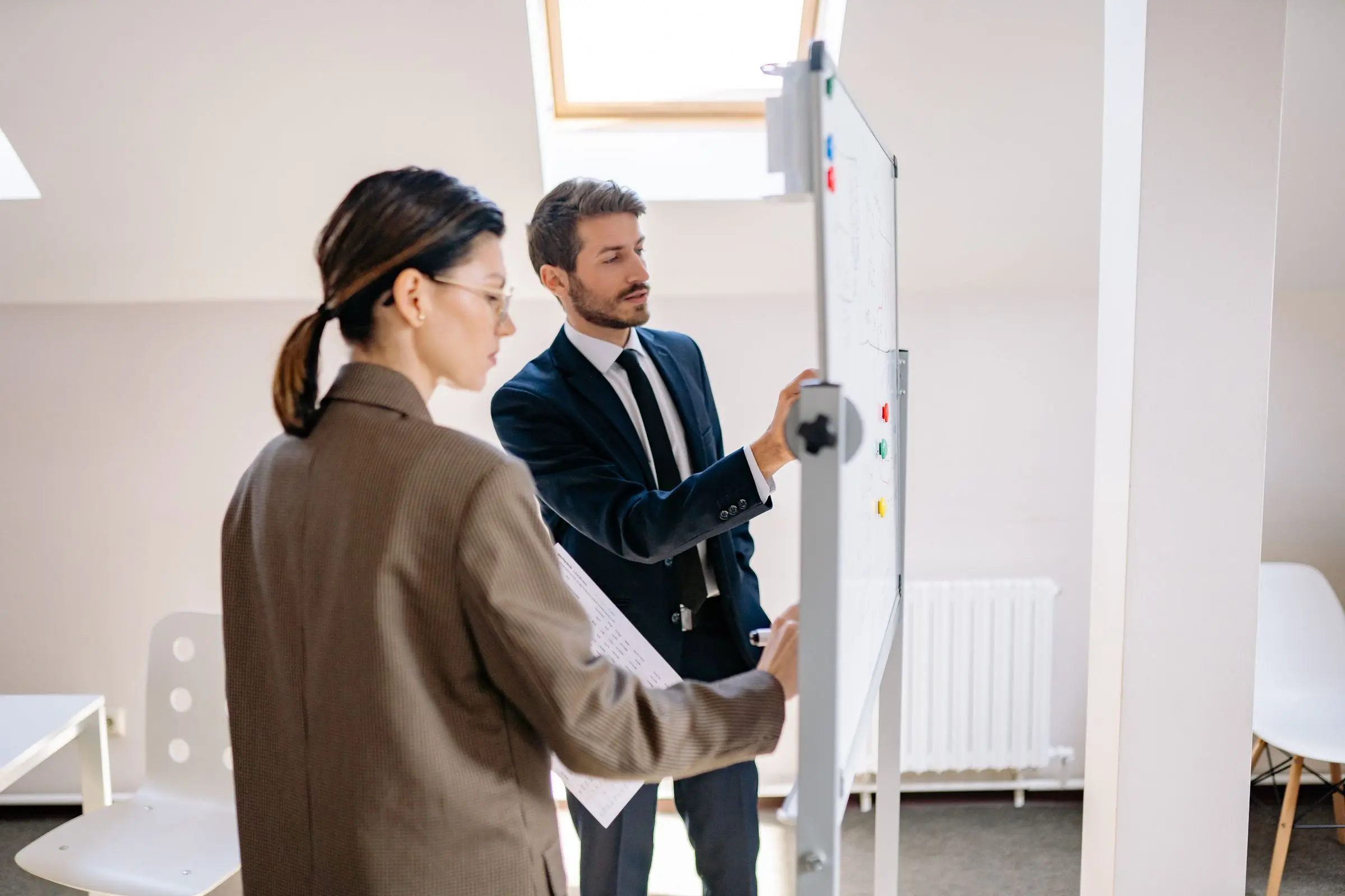 Two consultants working through a plan on a whiteboard in a bright office