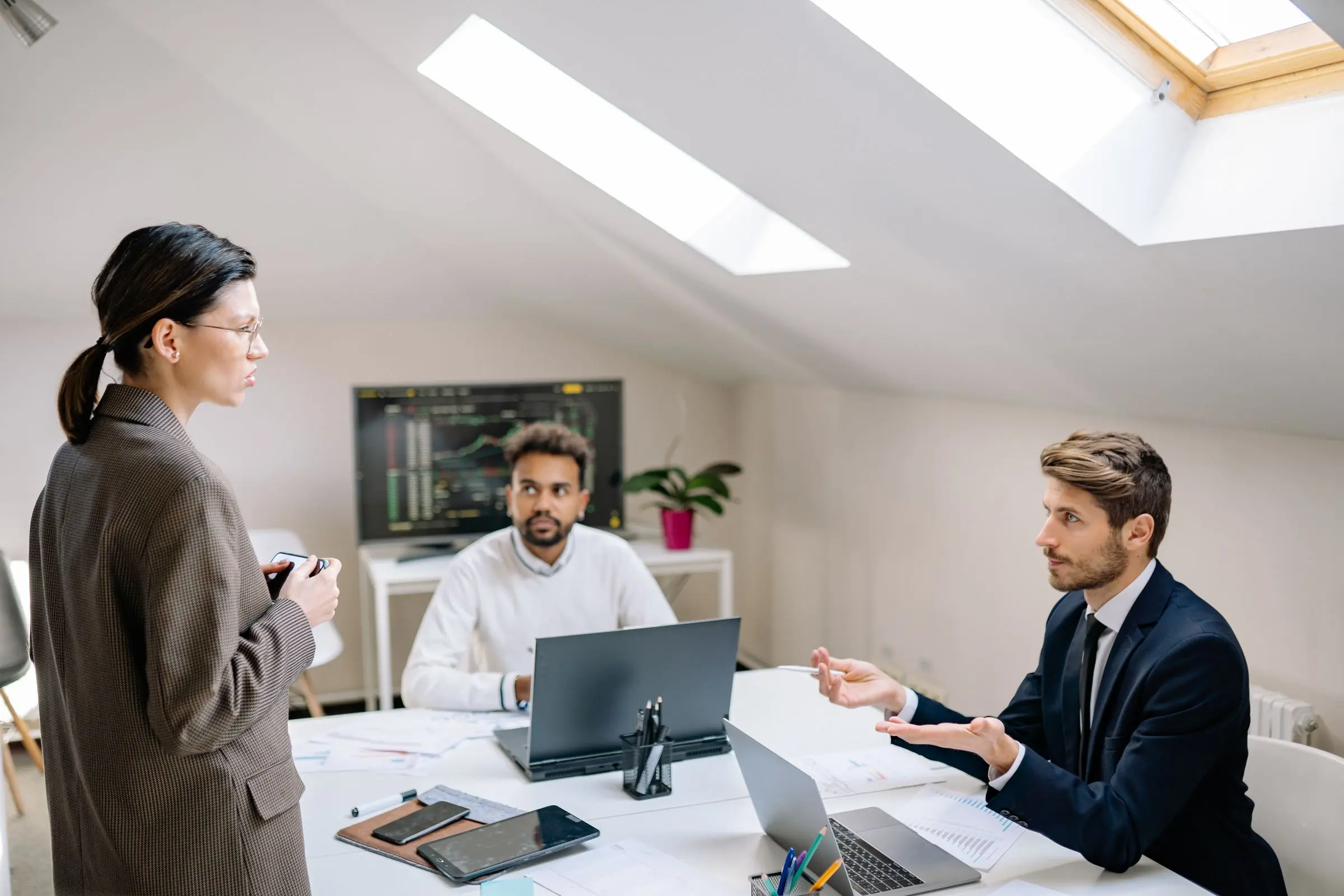 Three people in discussion around a laptop in a bright office under a skylight